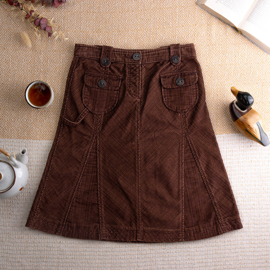 Vintage Timberland Corduroy A-Line Skirt – rich chocolate brown wide-wale corduroy, mid rise with double button waistband, two large front flap patch pockets with button closure, diagonal seam panelling, knee length A-line silhouette, gorpcore dark academia aesthetic, flat lay editorial shot