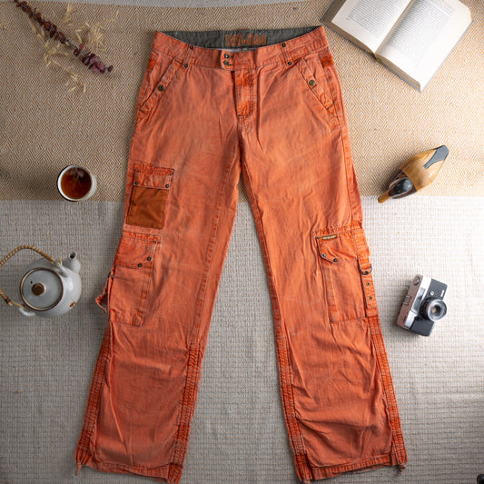 Vintage Mogul Y2K Orange Cargo Pants – washed burnt orange cotton, low rise double-button waist, multiple cargo pockets with mesh panel detail and snap closures, knee zip articulation, ankle zip hem, baggy cyber rave techwear silhouette, flat lay editorial shot