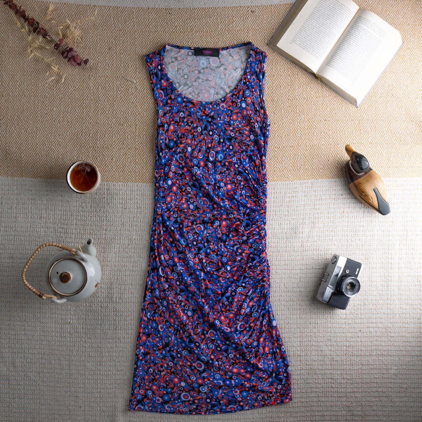 Vintage Versus Versace 90s Ruched Midi Dress – cobalt blue stretch mesh with all-over psychedelic pop art circle and star print in red, pink and white, scoop neckline, sleeveless, side ruching creating draped body-con silhouette, archival designer piece, flat lay editorial shot