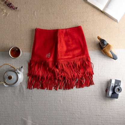 Vintage Blumarine Folies Y2K Red Suede Fringe Mini Skirt – vibrant red genuine leather suede, high waist, A-line silhouette with dramatic double-layer fringe hem, rhinestone crystal "B" logo detail at hip, western glam aesthetic, flat lay editorial shot