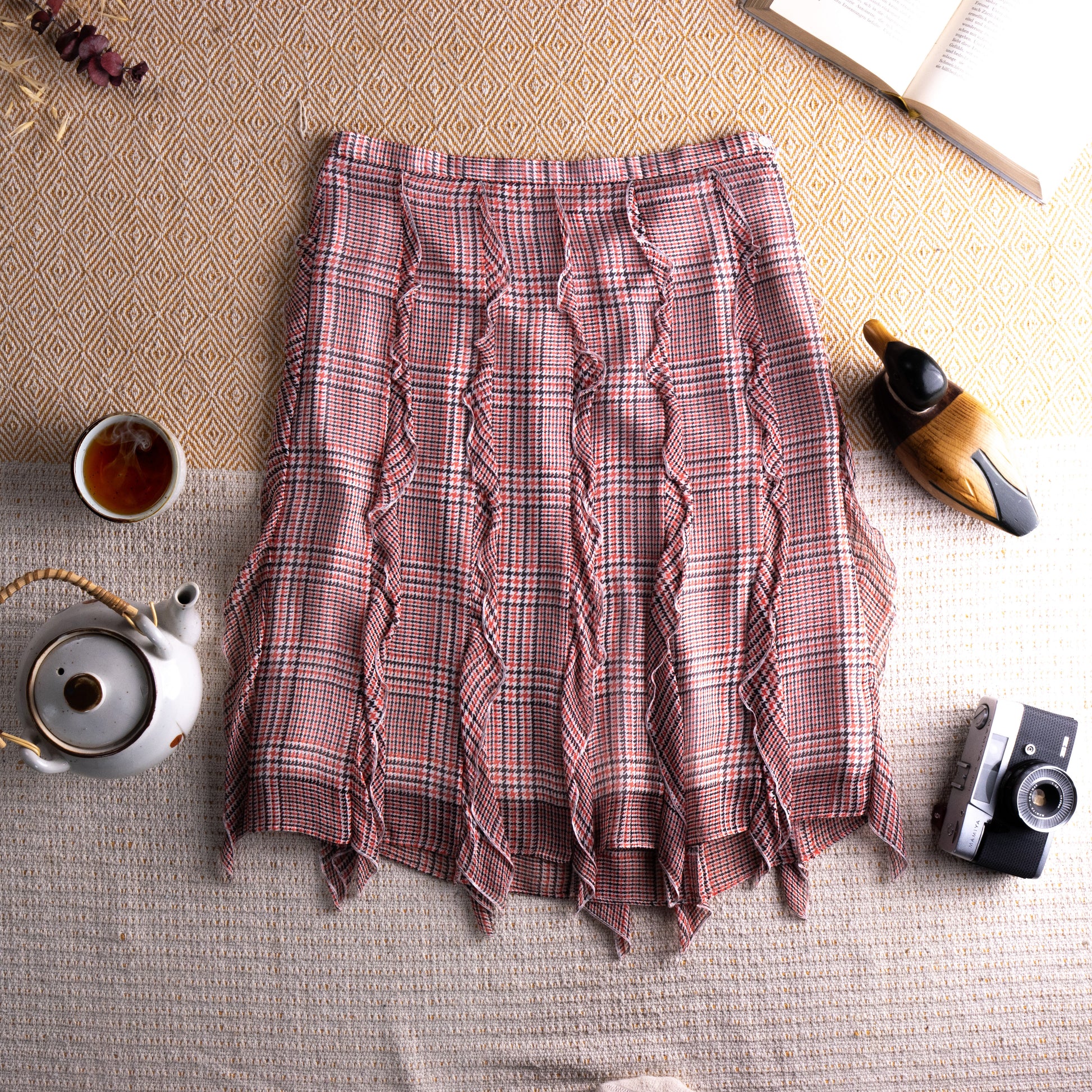 Vintage Cacharel Y2K Silk Ruffled Houndstooth Plaid Midi Skirt – blush pink, green and white houndstooth check silk, high waist, five vertical ruffle seam panels creating deconstructed avant-garde silhouette, raw fringe hem, A-line midi length, flat lay editorial shot