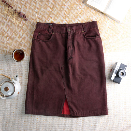 Reworked Versace Denim Midi Skirt – burgundy wine overdyed denim, mid rise with five-pocket construction and silver rivet hardware, pencil silhouette with deconstructed raw hem front slit revealing red lining, upcycled avant-garde grunge rework, flat lay editorial shot