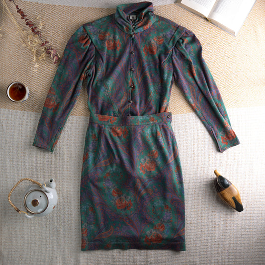Vintage Ungaro Parallèle Paris 80s Two-Piece Skirt Suit – emerald green, rust and mauve paisley floral jersey, high neck blouse with jewel button-front and dramatic puff shoulders, long sleeves, matching high-waist pencil midi skirt, Made in Italy, flat lay editorial shot