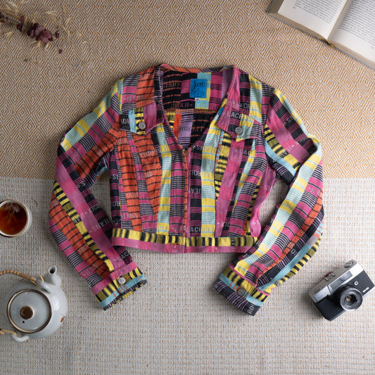 Christian Lacroix Jeans 90s Cropped Jacquard Jacket – bold multicolour striped jacquard with all-over "Lacroix Jeans" spellout logo repeat in pink, yellow, orange, sky blue and black, trucker-style collar, single-breasted button front, chest flap pockets, elasticated hem, long sleeves with button cuffs, maximalist rare archive piece, flat lay editorial shot