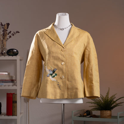 NOS Archival Kenzo Jungle Paris Deadstock 90s Yellow Linen Blazer – warm golden yellow linen, notch lapel, single-breasted with three mother-of-pearl buttons, 3D hummingbird and floral appliqué at lower front, long sleeves, fitted silhouette, product shot on dress form