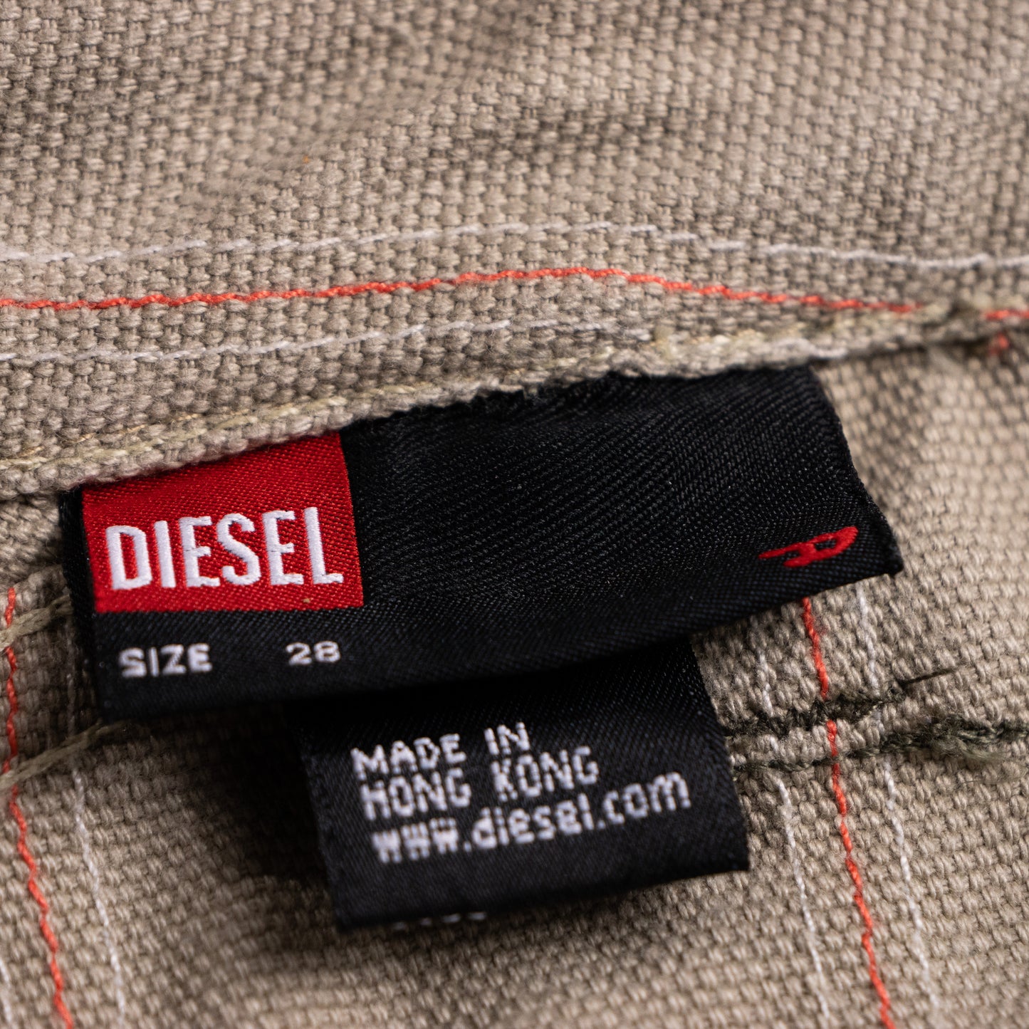 Close-up of the archival Diesel black interior clothing label with the iconic red square box logo, showing Size 28 and the secondary black tag reading Made in Hong Kong.

