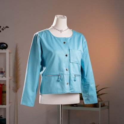 Archival André Courrèges aqua blue utility jacket from circa 1982, featuring a collarless boxy cropped silhouette, silver dome snap buttons, and signature zip pockets. Front view on mannequin, pristine museum grade condition.

