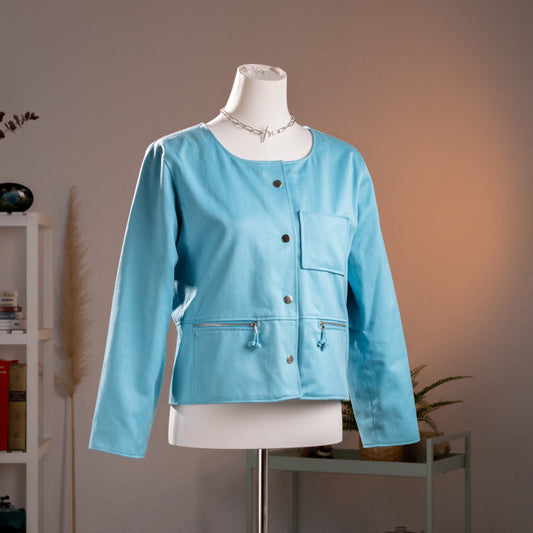 Archival André Courrèges aqua blue utility jacket from circa 1982, featuring a collarless boxy cropped silhouette, silver dome snap buttons, and signature zip pockets. Front view on mannequin, pristine museum grade condition.
