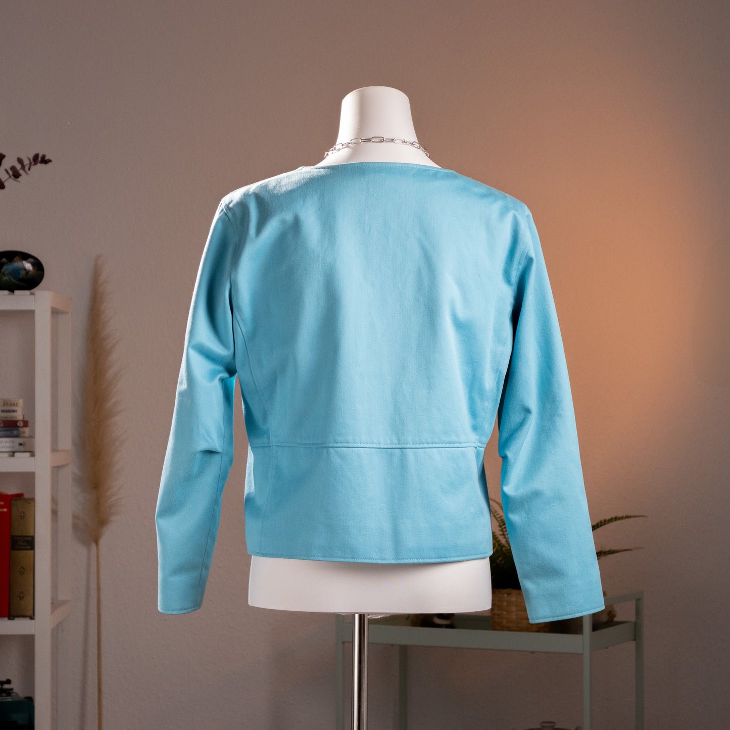 Full back view of the archival early 1980s Courrèges Paris aqua blue utility jacket on a mannequin, illustrating the stark horizontal panel construction and precise shoulder alignment.
