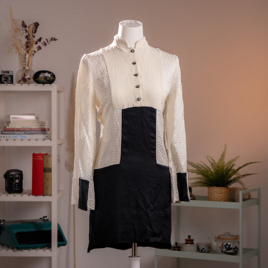 Front view of an archival Alexander McQueen ivory piqué and black silk runway dress from Fall Winter 2014 on a museum mannequin.