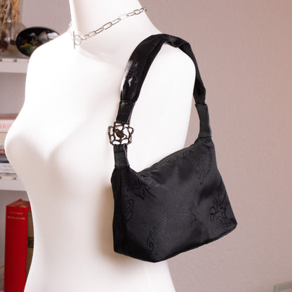Front profile of archival Blumarine black rose jacquard baguette bag on a museum mannequin, showcasing late 90s Anna Molinari shoulder bag silhouette.